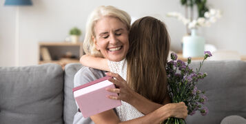 Happy,Senior,Grandma,Hugging,Granddaughter,Thanking,For,Present,Holding,Flower